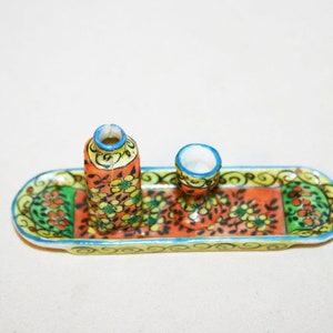 May include: A small, hand-painted ceramic tray with a floral design in shades of orange, green, and yellow. The tray features two small ceramic containers, one tall and one short, with matching floral designs.