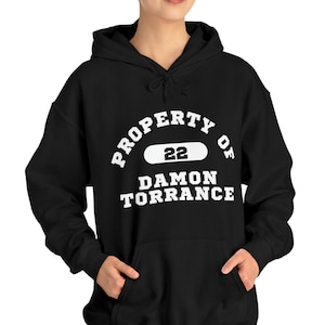以下が含まれることがあります： 「PROPERTY OF 22 DAMON TORRANCE」という白い文字が書かれた黒いフード付きスウェットシャツ。