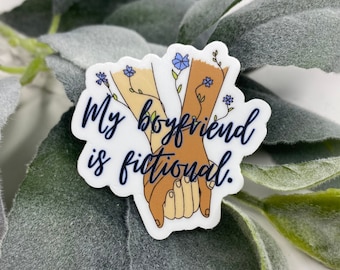 May include: A white sticker with a blue and brown illustration of two hands holding each other. The text "My boyfriend is fictional." is written in blue cursive lettering.