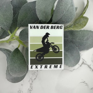 May include: A rectangular sticker featuring a silhouette of a person on a dirt bike performing a stunt. The sticker has a striped background in shades of green. The text "VAN DER BERG EXTREME" is printed in white.