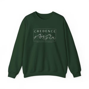 May include: A dark green sweatshirt with a white graphic design. The graphic features a mountain range with the text "CREDENCE" and the phrase "Believe us in the truth of something".