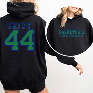 May include: Black hoodie with the name "CRIST" in blue lettering above the number "44" in green with a blue outline. The hoodie also features text that reads "Basketball State Champions" in green and blue.