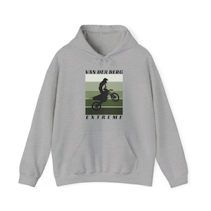 May include: A gray hooded sweatshirt with a graphic print of a person riding a dirt bike. The graphic is in a retro style with green, white, and black colors. The text "VAN DER BERG EXTREME" is printed below the graphic.