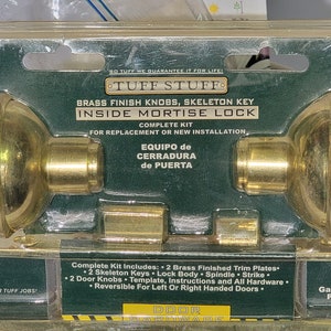 以下が含まれることがあります： 骨組みキー付きの真鍮仕上げのドアノブセットが入ったパッケージ。パッケージは緑と金で、「タフスタッフ」と「No. 1200」の文字が書かれている。パッケージには、ドアノブ2個、骨組みキー2個、ロックボディ、スピンドル、ストライク、テンプレート、説明書、すべての金具が含まれている。ドアノブセットは、左右どちらのドアにも対応している。