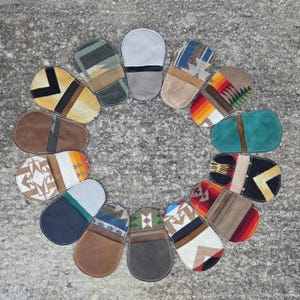 May include: A circular arrangement of various small, oval-shaped leather goods. Each item features a unique combination of colors and patterns, including geometric designs, stripes, and solid color blocks. The items are likely small pouches or cases.