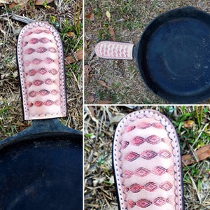 May include: A close-up of a cast iron skillet with a leather handle cover. The cover is pink and has a geometric pattern. The skillet is black and has a rough surface.