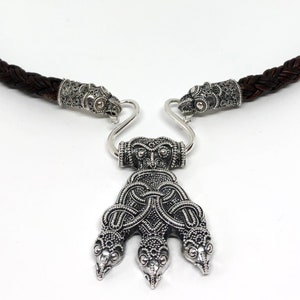Può includere: Una collana d'argento con un cordoncino in pelle marrone intrecciato e un ciondolo con un design a serpente a tre teste.