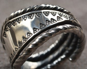 Peut inclure: Une bague en argent avec une bande torsadée et un motif décoratif de triangles et de points.