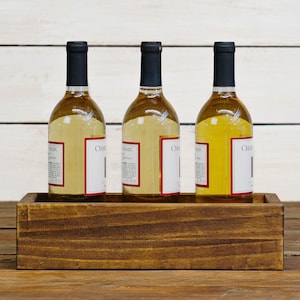 May include: Three bottles of white wine in a wooden crate. The bottles are labeled "Chardonnay".
