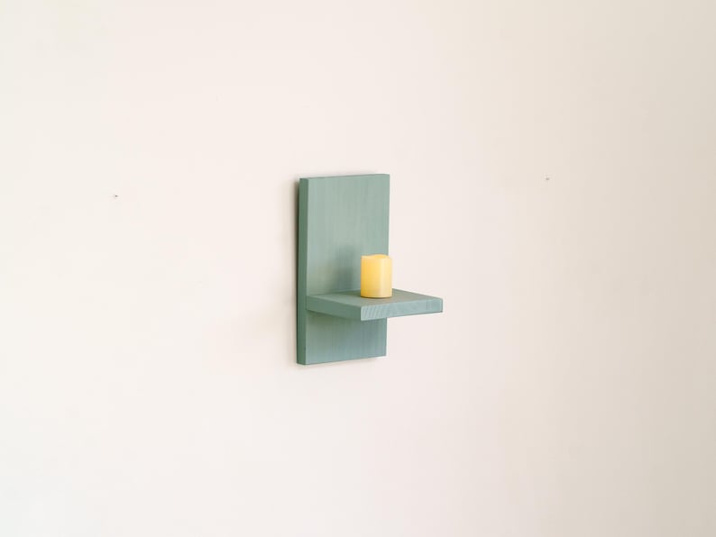 May include: A wall-mounted teal wooden shelf with a small, yellow candle. The shelf has a rectangular back and a small, horizontal platform. The candle is cylindrical. The shelf is a decorative item.