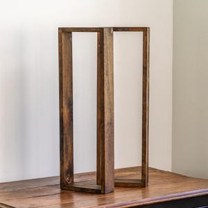 May include: Two dark brown wooden decorative frames. The frames are rectangular and stand upright on a wooden table. The wood grain is visible, adding texture to the design. The background is a plain white wall.