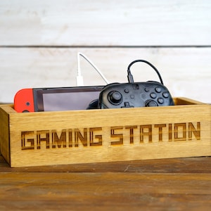 May include: A wooden box with the words "Gaming Station" engraved on the front. The box contains a video game console and a controller.