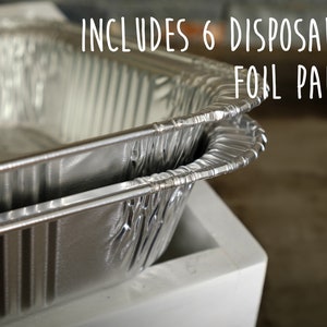 May include: Two silver aluminum foil pans stacked on top of each other. The text "INCLUDES 6 DISPOSABLE FOIL PANS!" is written in white on a black background above the pans.