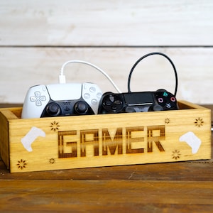 May include: A wooden box with the word "GAMER" engraved on the front. The box has two video game controllers inside, one white and one black.