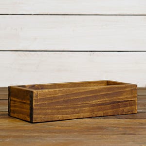 May include: A rectangular wooden box with a dark brown stain. The box has a slightly raised edge around the top and is made of wood planks.