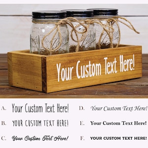 May include: A wooden box with three glass jars with black lids and twine tied around the tops. The box has the text "Your Custom Text Here!" printed on the front.