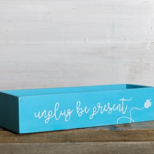 May include: A light blue wooden box with the words "unplug be present" and a stylised image of an electrical cord and plug painted in white.