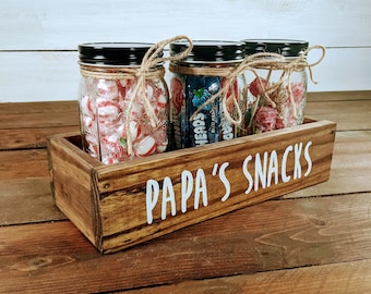 May include: A wooden box with the words "Papa's Snacks" on the front. The box contains three glass jars filled with different types of sweets.