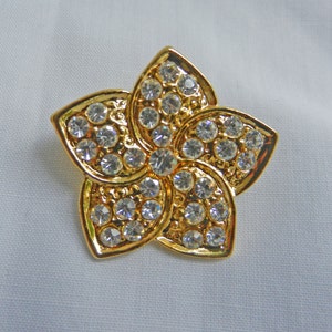 May include: A gold-toned flower brooch with clear rhinestones. The brooch is shaped like a five-pointed star.
