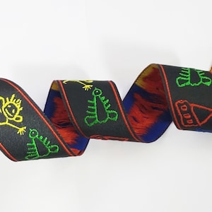 May include: Black ribbon with colorful embroidered designs of stick figures, a house, and a worm. The ribbon has a red, blue, and yellow fringe.