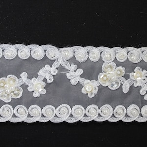 May include: White lace trim with a scalloped edge and pearl beads. The trim features delicate floral designs with small pearl accents.