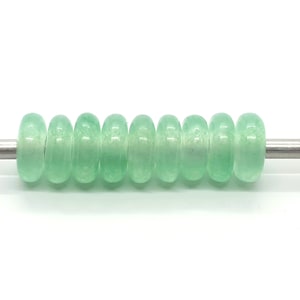 May include: A strand of ten light green jade donut beads on a silver rod.