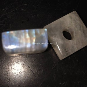 Puede incluir: Dos piezas de piedra lunar, una es un prisma rectangular con un agujero en el centro, la otra es un rectángulo liso y redondeado.