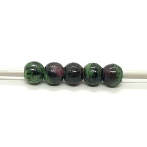 May include: A strand of six green, black, and pink gemstone beads on a white string.