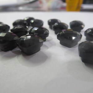 May include: A group of 12 black faceted glass buttons. The buttons are all the same size and shape, and they have a shiny finish.