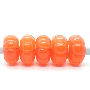 Könnte beinhalten: Fünf orangefarbene Glasperlen mit strukturierter Oberfläche, auf einer weißen Schnur aufgefädelt.