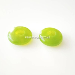 May include: Two green jade donut beads with a hole in the center. The beads are smooth and polished.