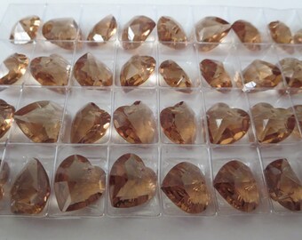 May include: A clear plastic tray filled with faceted, amber-coloured crystal beads. The beads are in various shapes, including teardrops and hearts. The crystals are arranged in individual compartments.