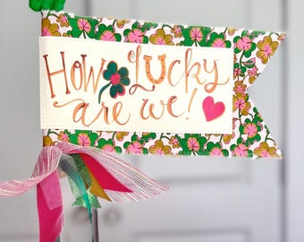Quelle chance avons-nous ! Drapeau Aimee Ferre Celebration sur tissu vert, rose vif et doré avec des trèfles