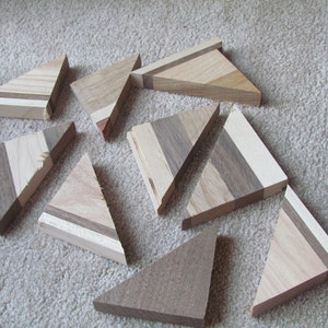 May include: A set of ten wooden triangle shapes, each made of different wood types and colors. The triangles are arranged in a random pattern on a light brown carpet.