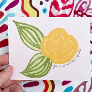 May include: A yellow flower with green leaves on a white background. The text "you are wildly capable" is written in black cursive.