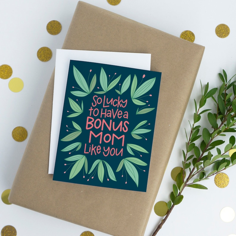 Puede incluir: Una tarjeta azul oscuro con hojas verdes alrededor del borde. La tarjeta dice "So lucky to have a bonus mom like you" en letras blancas y rosas.