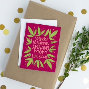 May include: A pink card with green leaves around the edges. The card says "So lucky to have an amazing mom like you!"