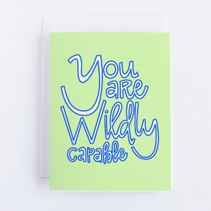 May include: A greeting card with a light green background and the words "You are Wildly Capable" in blue script. The card is set against a white background.