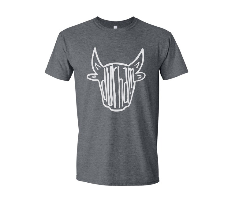 May include: A dark heather grey t-shirt with a white bull head graphic. The bull's head is made up of the word "Durham".