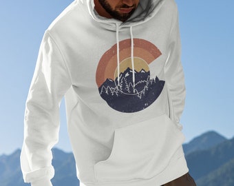 Puede incluir: Sudadera con capucha blanca con un gráfico de estilo vintage de una cordillera y una puesta de sol en un círculo. El gráfico está en tonos de azul, naranja y amarillo.