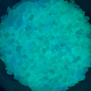 May include: A close-up of a pile of teal and blue glow-in-the-dark crystals.