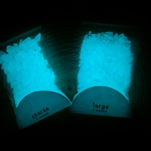 May include: Two bags of glowing, light blue, coarse and large crystals. Each bag is labeled with "1 ounce". The crystals are in clear plastic bags with a white label.