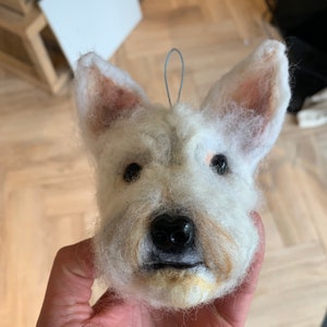 May include: A white felt sculpture of a dog's head with brown ears and a black nose.
