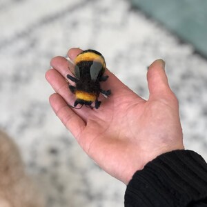 May include: A hand holding a black and yellow felt bumble bee toy with clear plastic wings.