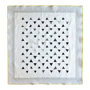 May include: A white quilt with a yellow border and a pattern of black triangles.
