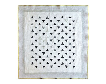 May include: A white quilt with a yellow border and a pattern of black triangles.