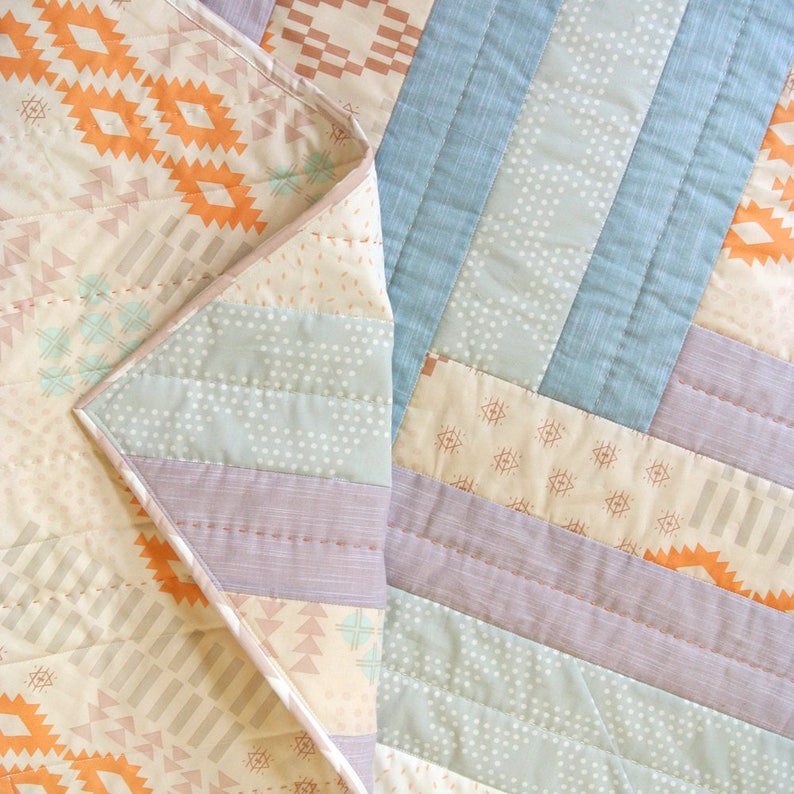 May include: A quilt with a patchwork design featuring various shades of blue, purple, orange, and beige. The quilt is made of different fabrics with geometric patterns and textures.