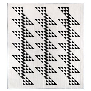 Puede incluir: Colcha de patrón geométrico en blanco y negro con un diseño en zigzag. La colcha está hecha de cuadrados de tela cosidos juntos para crear un patrón repetitivo.