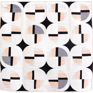 Op de afbeelding: Een wit quilt met een geometrisch patroon van zwarte en roze cirkels. De cirkels zijn gerangschikt in een rasterpatroon en elke cirkel heeft een ander geometrisch ontwerp erin.