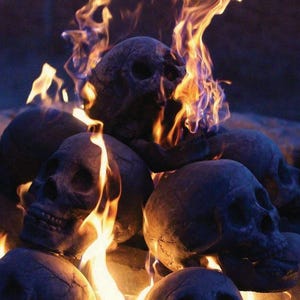 May include: A pile of dark gray skull-shaped objects with flames rising from them. The flames are orange and yellow, creating a dramatic contrast against the skulls. The scene evokes a Halloween or gothic theme.